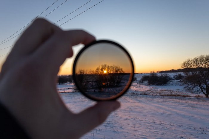 Hand holding a lens filter in front of the sun in snowy landscape