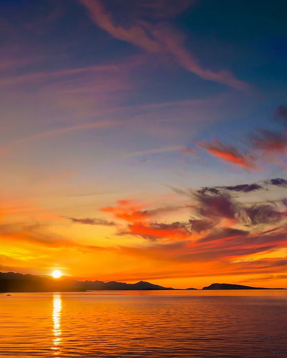 Sun setting over distant hills with the sea in the foreground 