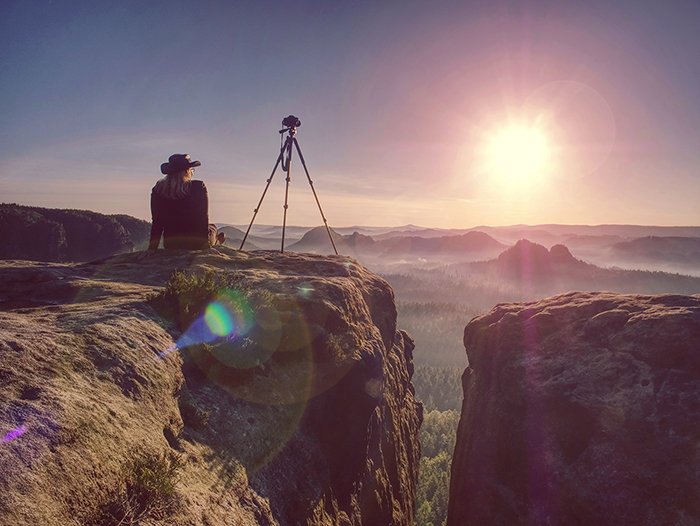 photographer sitting on a mountain with a tripod in the sunset