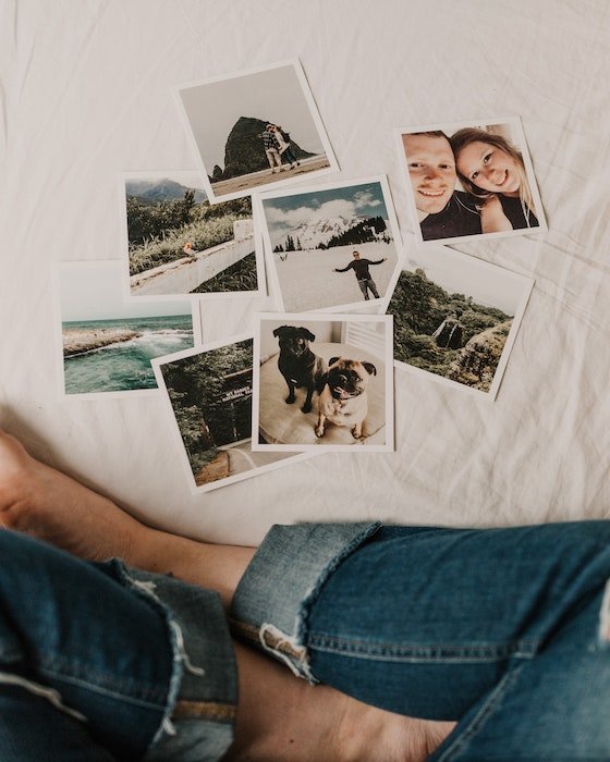 Printed square format glossy photos displayed in front of person sitting on a bed
