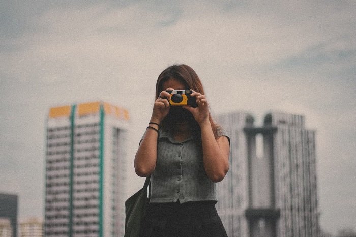 Woman taking picture with a disposable camera in front of two tall buildings 