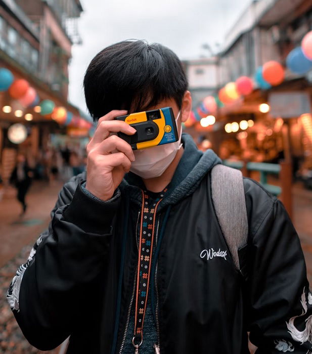 Man holding a disposable camera to his face in a market