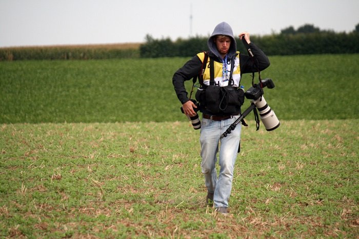 Man walking through a field carrying lots of camera equipment