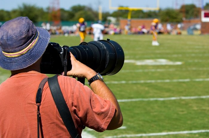 Man in a bucket hat taking pictures of a sports even with a telephoto lens