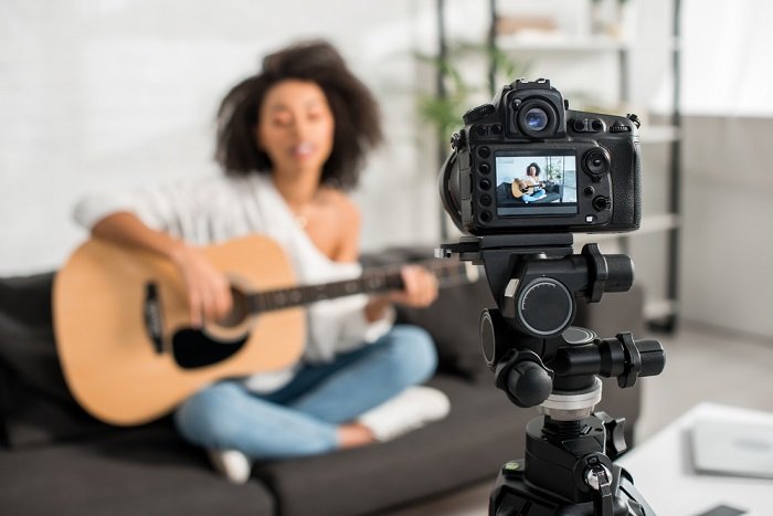 Camera on a tripod set up in front of a woman on a sofa playing the guitar