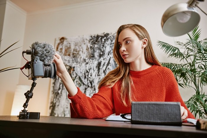 Woman in red jumper adjusting a camera situated on the desk beside her