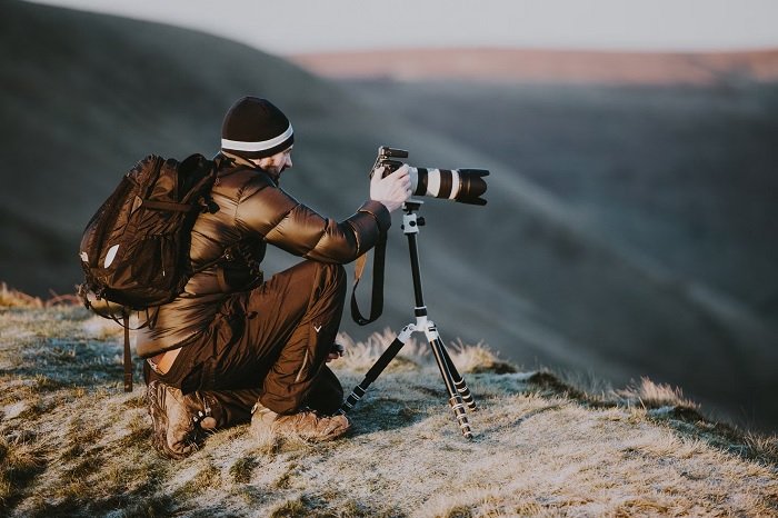 Man on a hilltop taking a picture with a camera on a tripod