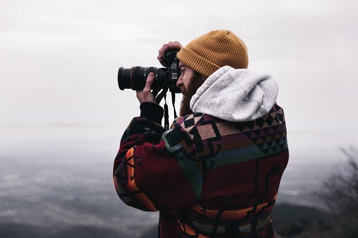 Man in a big fleece taking a picture with a camera