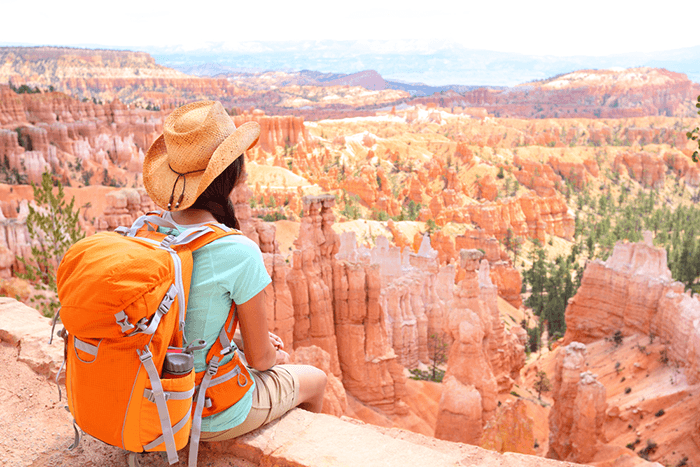 Woman with camera bag sitting at the edge of a canyon