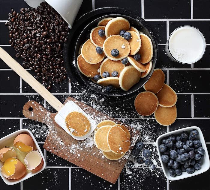 Flat lay of pancakes and ingredients on black tiles