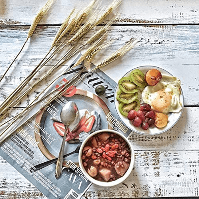 Flat lay of a magazine, wheat, and breakfast food on a white wood background