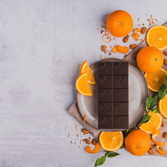 在水泥食物摄影背景上，盘子上放着平坦的橘子和巧克力