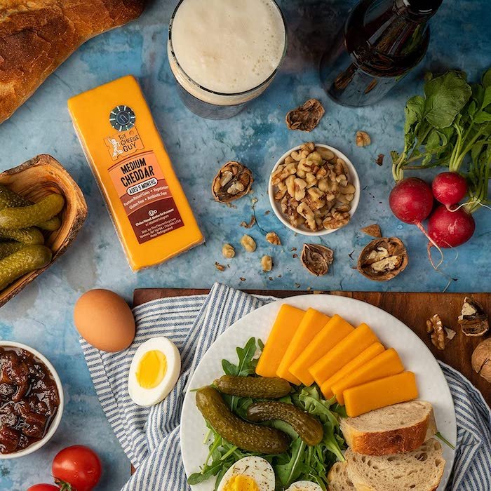 Flat lay of cheeses, nuts, eggs, and vegetables on a blue food backdrop