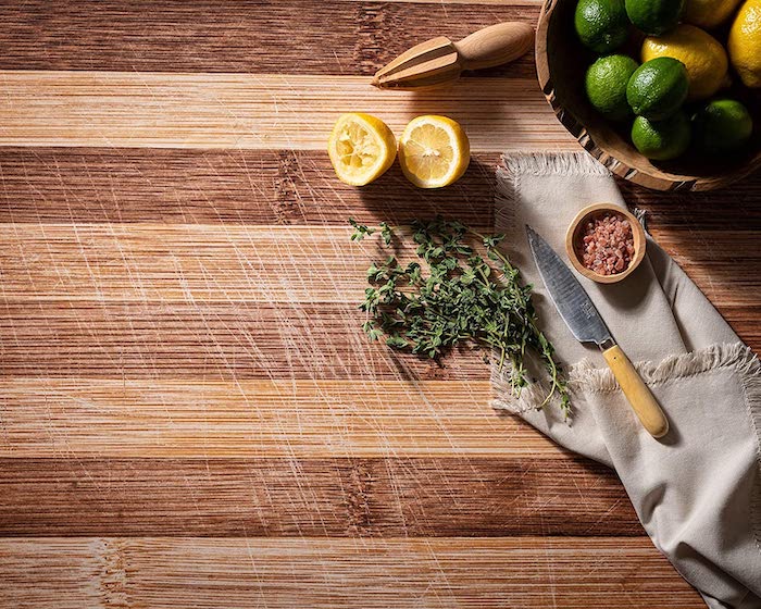 A knife, herbs, lemons, and limes on a wooden cutting board