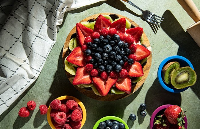 A flat lay shot of a fruit tart and bowls of fruit around it