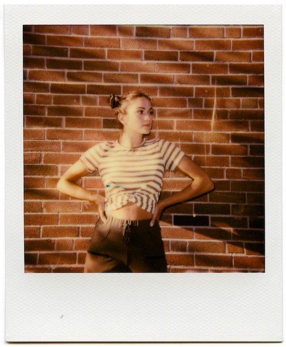 Polaroid picture of a girl standing by wall 