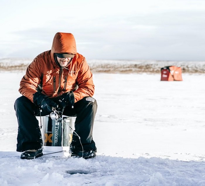Man in orange coat fishing through hole in the ice