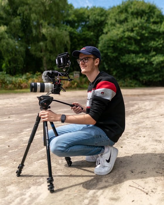 Man crouching down to use a camera on a video tripod
