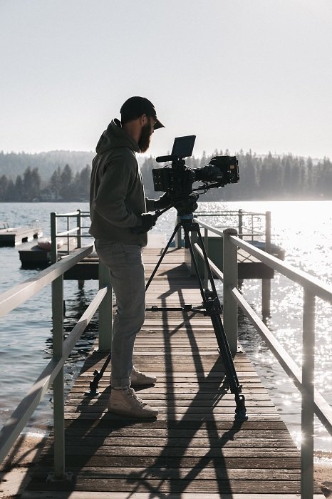 Man in a cap using a video camera on a tripod on a pier