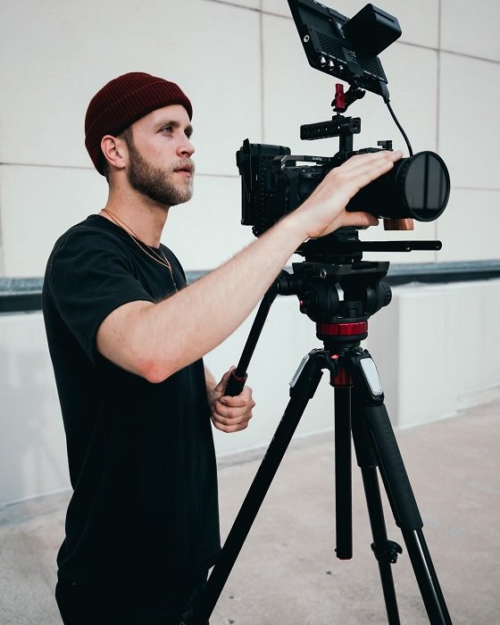 Man in a woolly hat using a large camera on a tripod