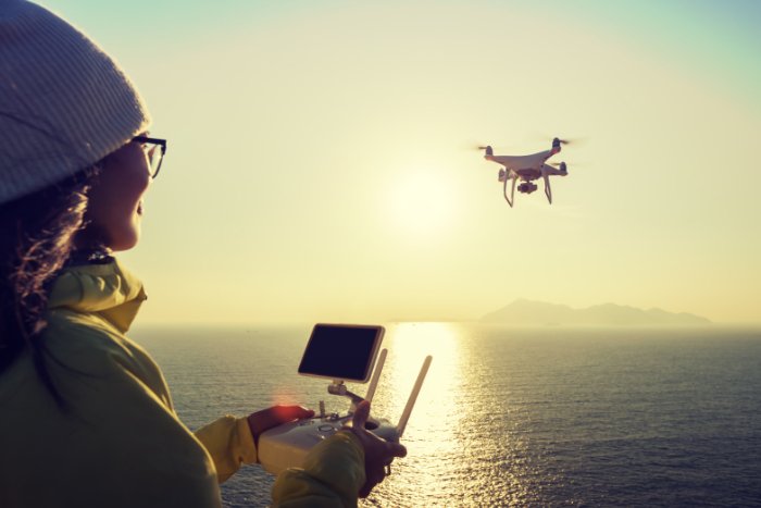 woman flying a drone over the sea at sunset