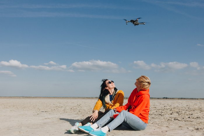 Two women sitting on a beach flying a drone