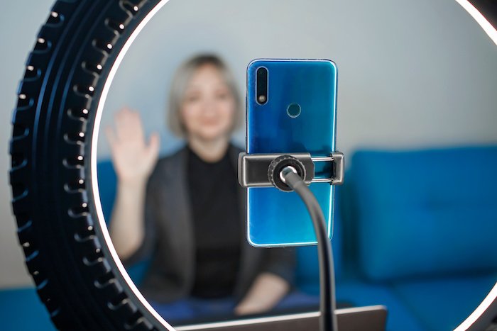 Business woman in a zoom meeting with a smartphone and ring light lamp at home