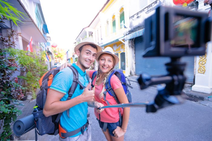 Young backpacking couple take a selfie on the street with an action camera and selfie stick 