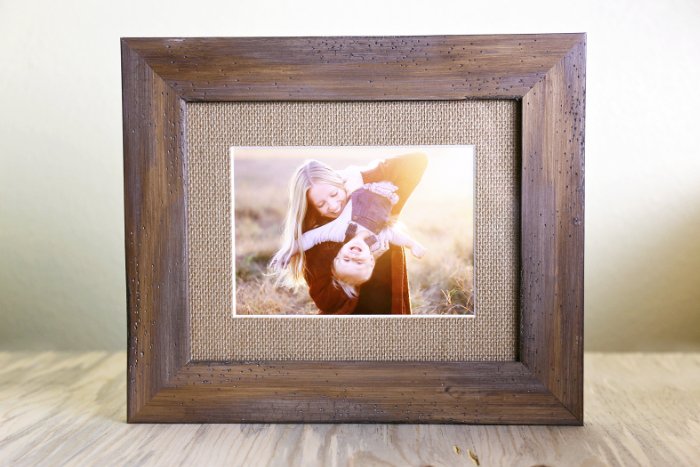 Wooden photo frame with hessian mount standing on a wooden table and a picture of mother and child 
