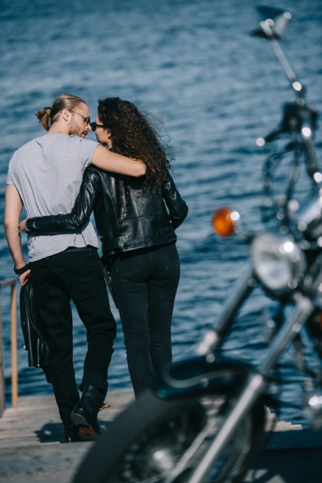 Couple by the sea, arms around each other, with their motorbike in the foreground