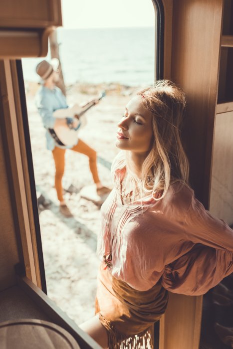 Young woman in doorway, with an out-of-focus man outside playing the guitar