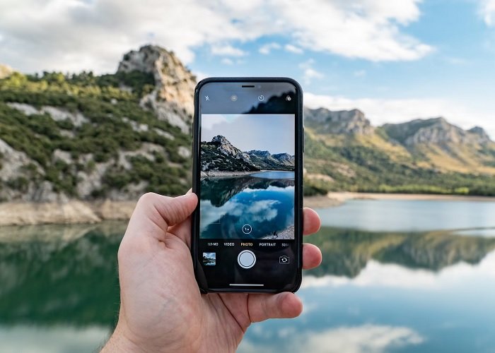 Hand holding an iPhone to take a picture of a lake