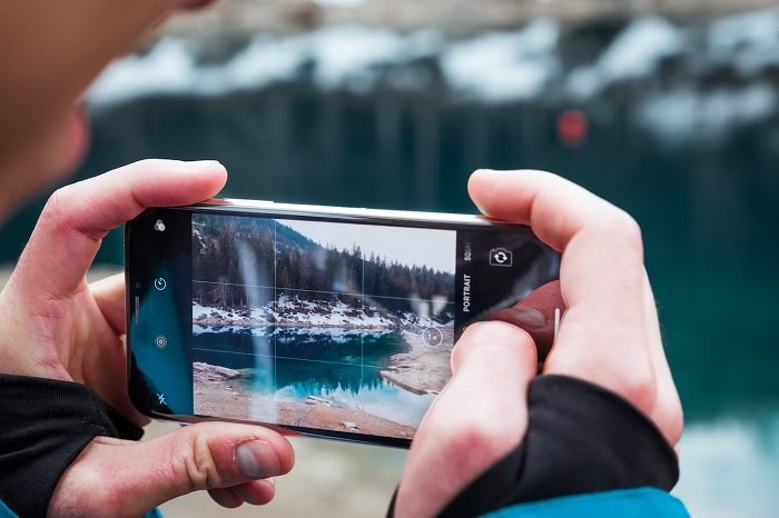 Pair of hands holding a smartphone camera for a picture of a lake landscape