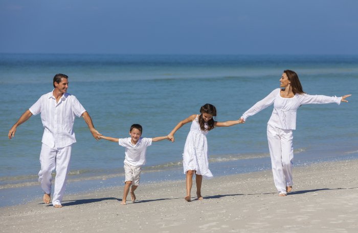 A summer family photo on the beach with parents and kids holding hands