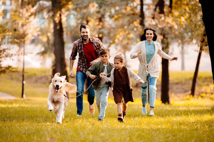 A family of four running in a park with their dog