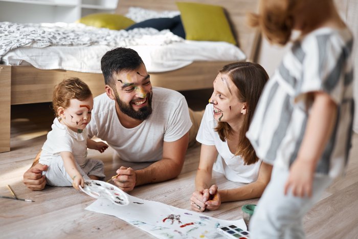 A family dressed in white painting together on floor with paint on their faces