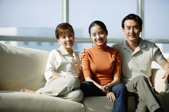 A family in neutral-color clothing sitting on a couch