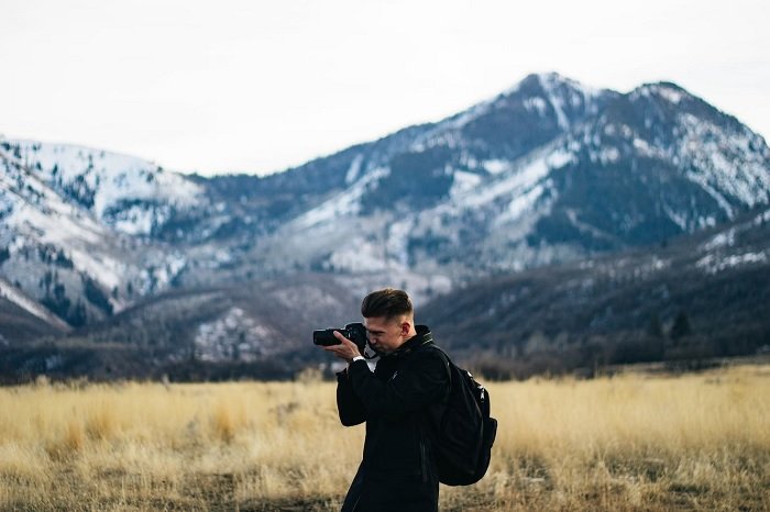 Man with a camera and camera bag taking a picture in a mountain landscape