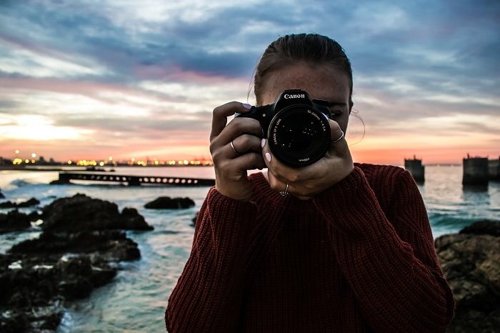 Woman in red jumper taking a picture with a canon camera on the shore