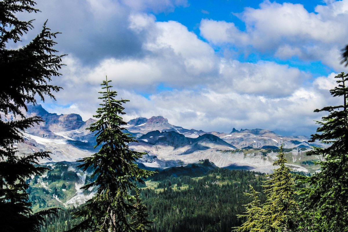 A mountain landscape with a blue sky and white clouds with trees in the foreground shot with one of the best affordable cameras for landscape photography