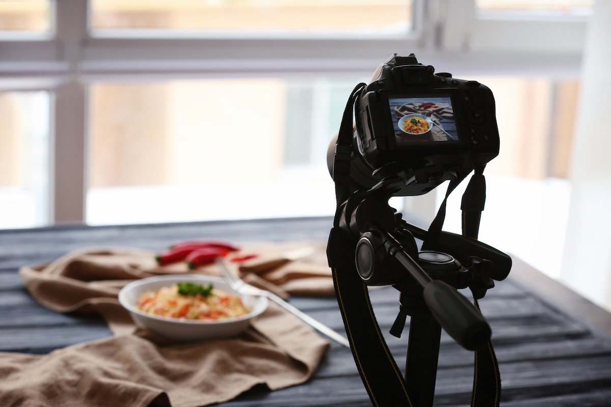 A tripod with a camera for food photography on it taking a picture of food in a bowl on a table by a window