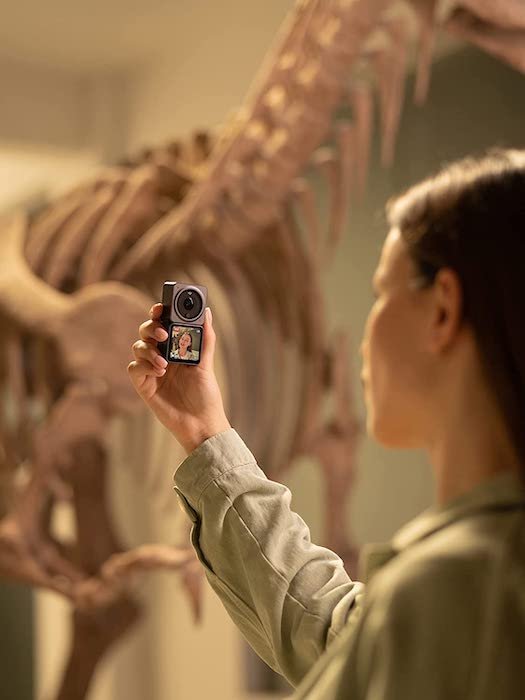 Woman taking a selfie with the DJI Action 2 GoPro alternative with a dinosaur skeleton in the background
