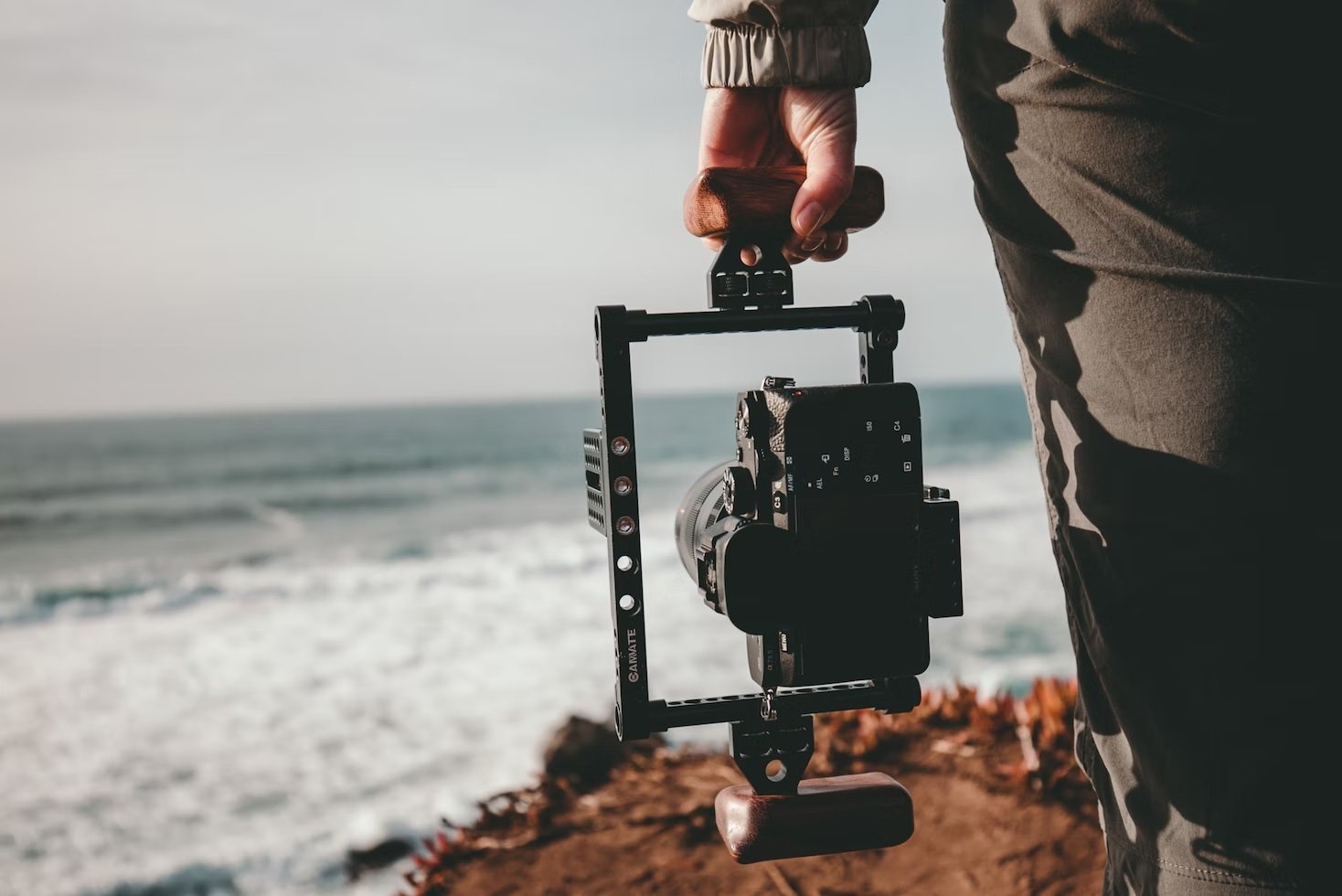 Hand holding a camera in a camera stabilizer cage on the beach