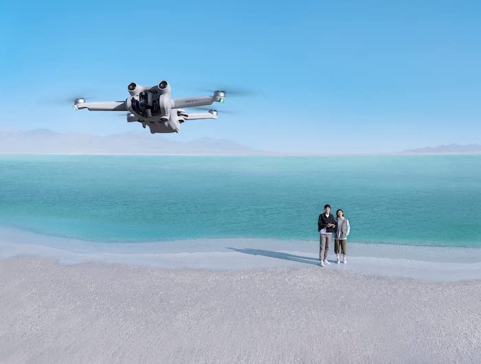 A couple flying the DJI Mini 3 Pro on a beach by water