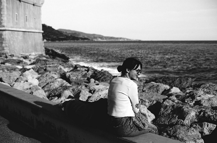 Woman sitting on concrete by the sea shot on Lomography Fantome Kino 8