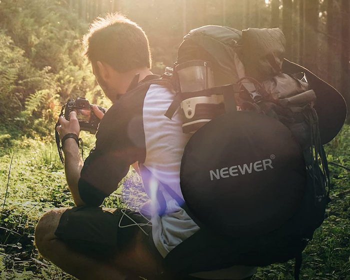 A photographer taking pictures in nature with a Newer reflector strapped to his backpack