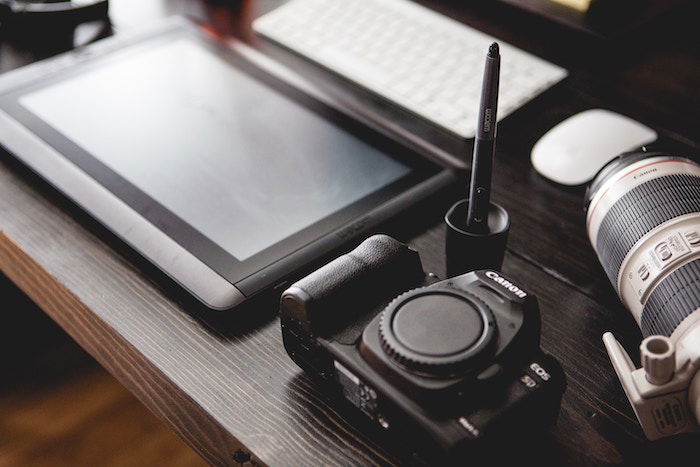 A Wacom tablet and pen on a desk with a Canon camera and lens