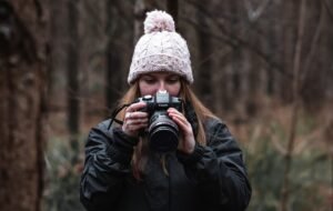 Woman in woolly hat looking at the back of a camera in a forest