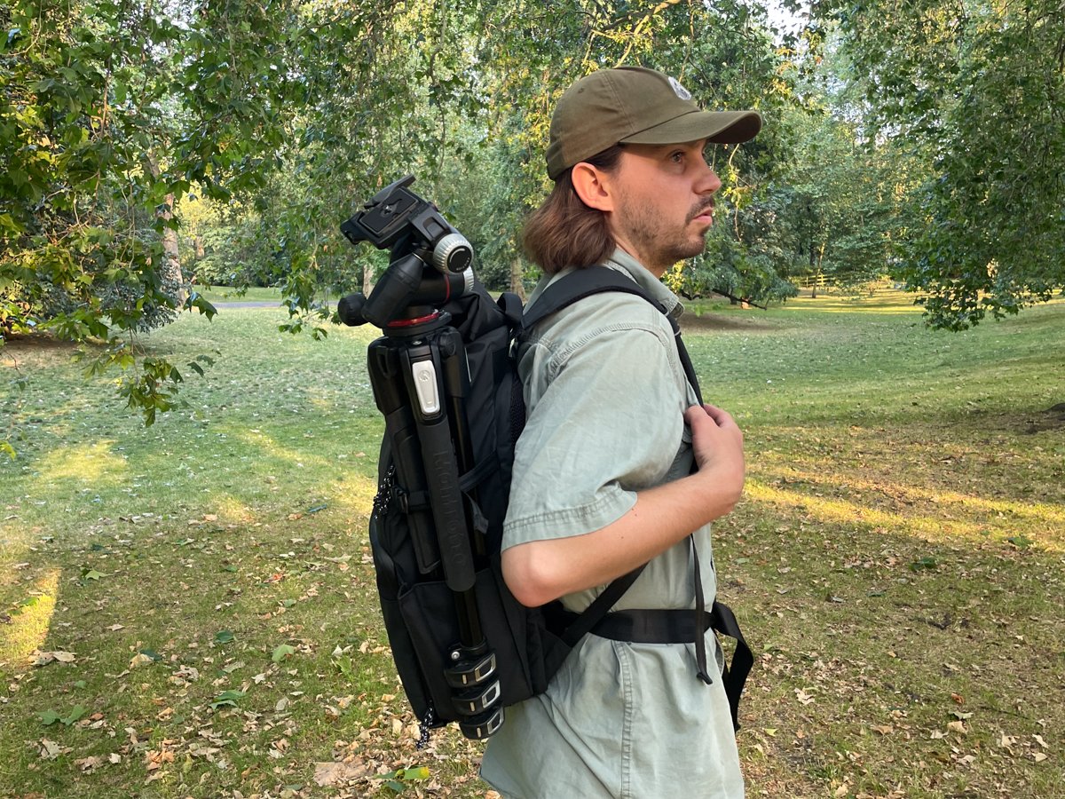 A person wearing the Tenba DNA with a tripod attached to its side
