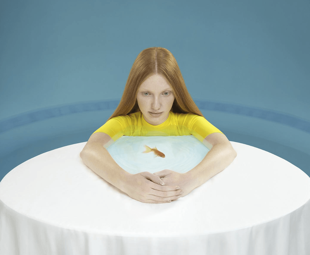 A girl with her arms stretched in a circle on a table with a goldfish